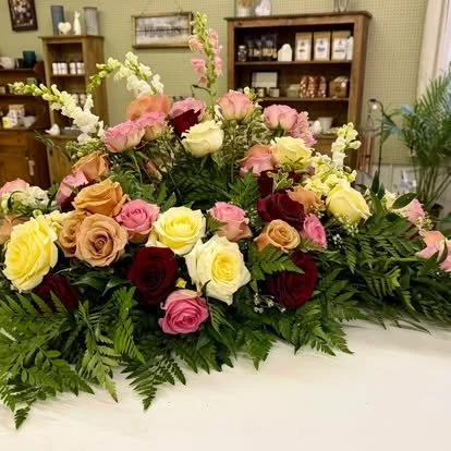 A large floral arrangement of pink, yellow, cream, and deep red roses with green foliage on display in a store.