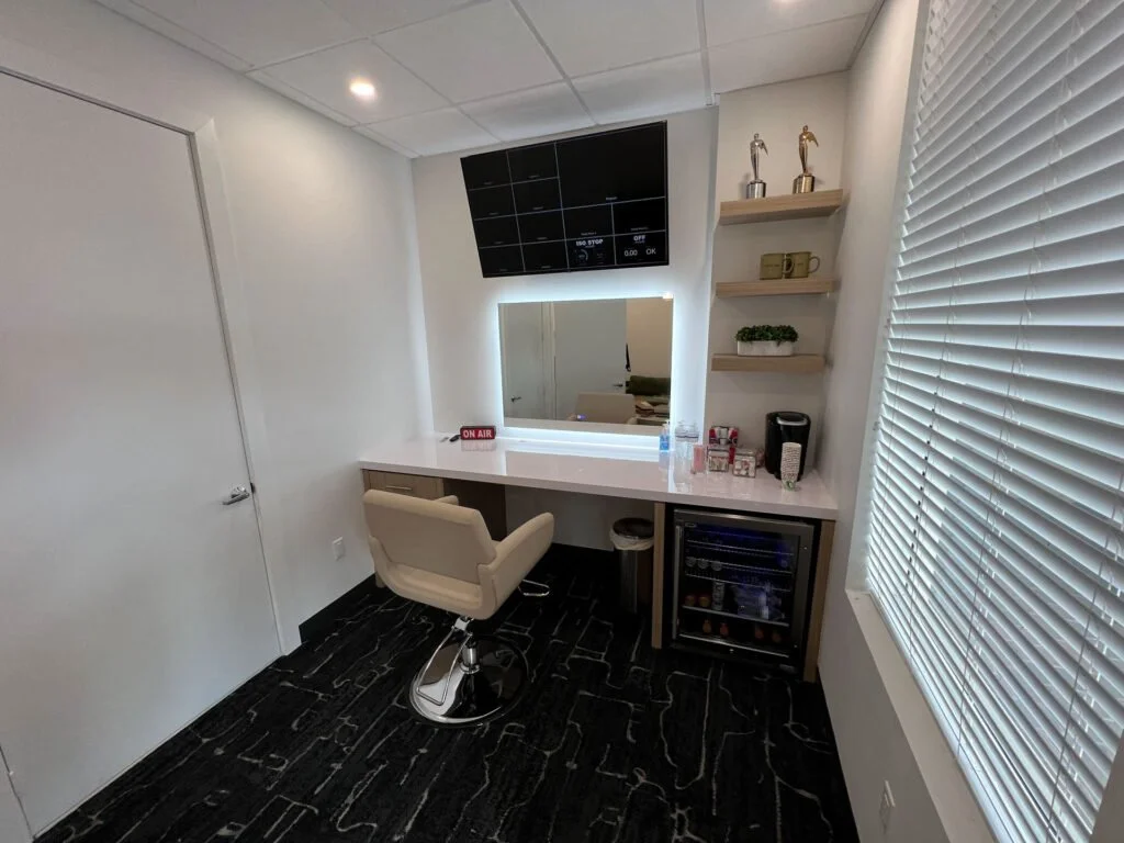 Small office or makeup room with a desk, chair, mirror, shelves, a beverage cooler, and some decor items.