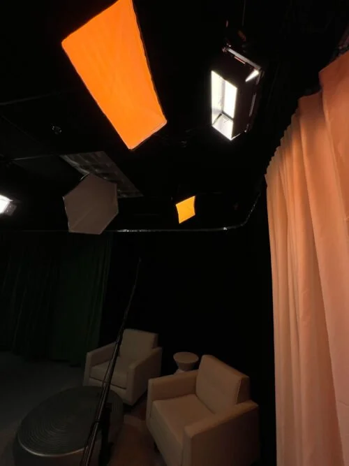 TV studio with black walls, studio lights on the ceiling, chairs, and curtains.