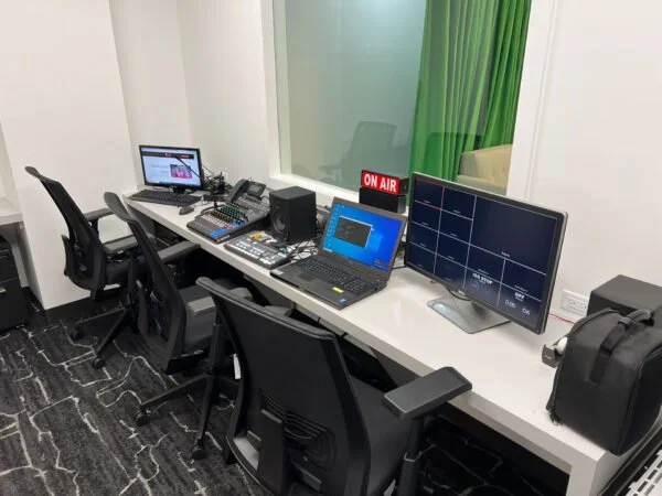 Radio station control room with multiple monitors, audio equipment, a laptop, and an