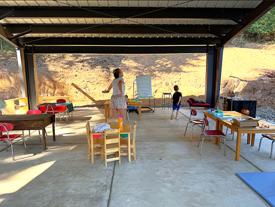 A guide and student at Growing Montessori outdoor school in Woodland, Wa. Outdoor classroom with Montessori based toys and activities under a covered patio with the sun shining through