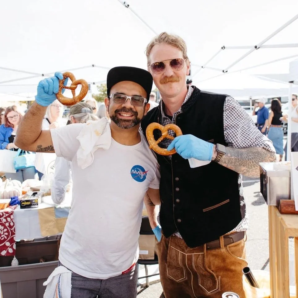 Two bakers holding up pretzels and smiling to the camera