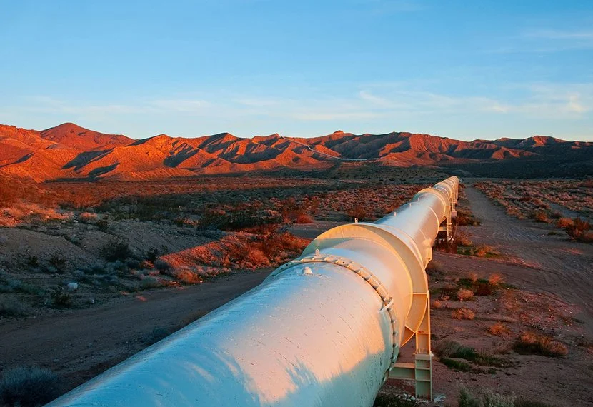 A long pipeline running through a desert landscape with hills in the background during sunset.