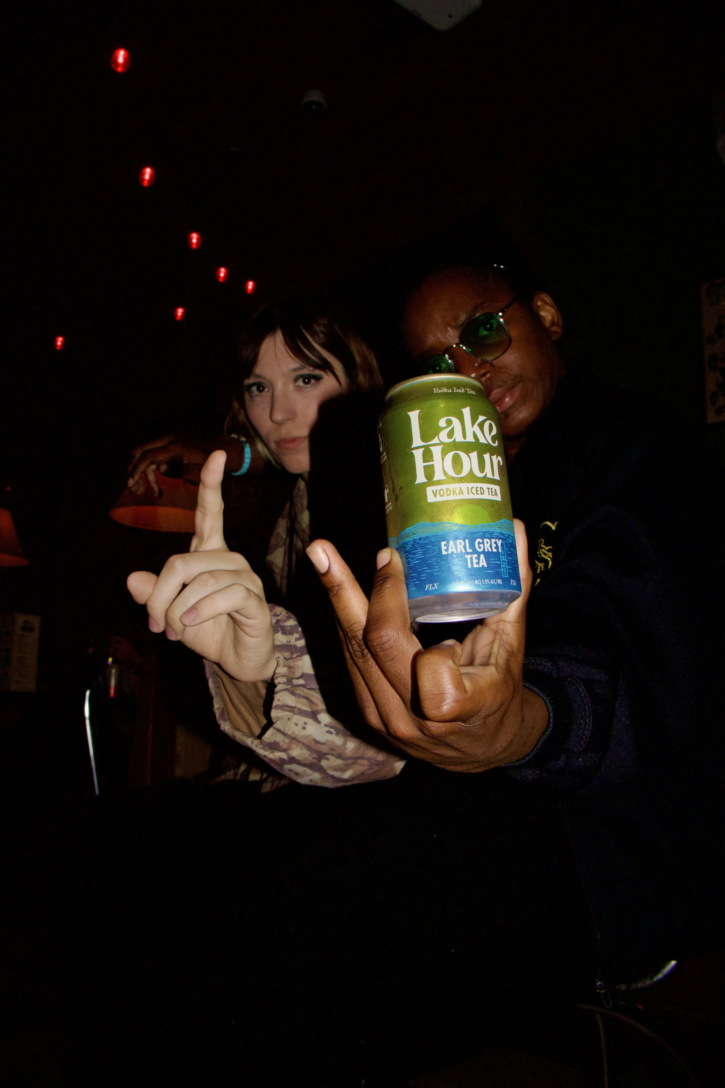 Two people in a dark room holding an Earl Grey tea can labeled Lake Hour