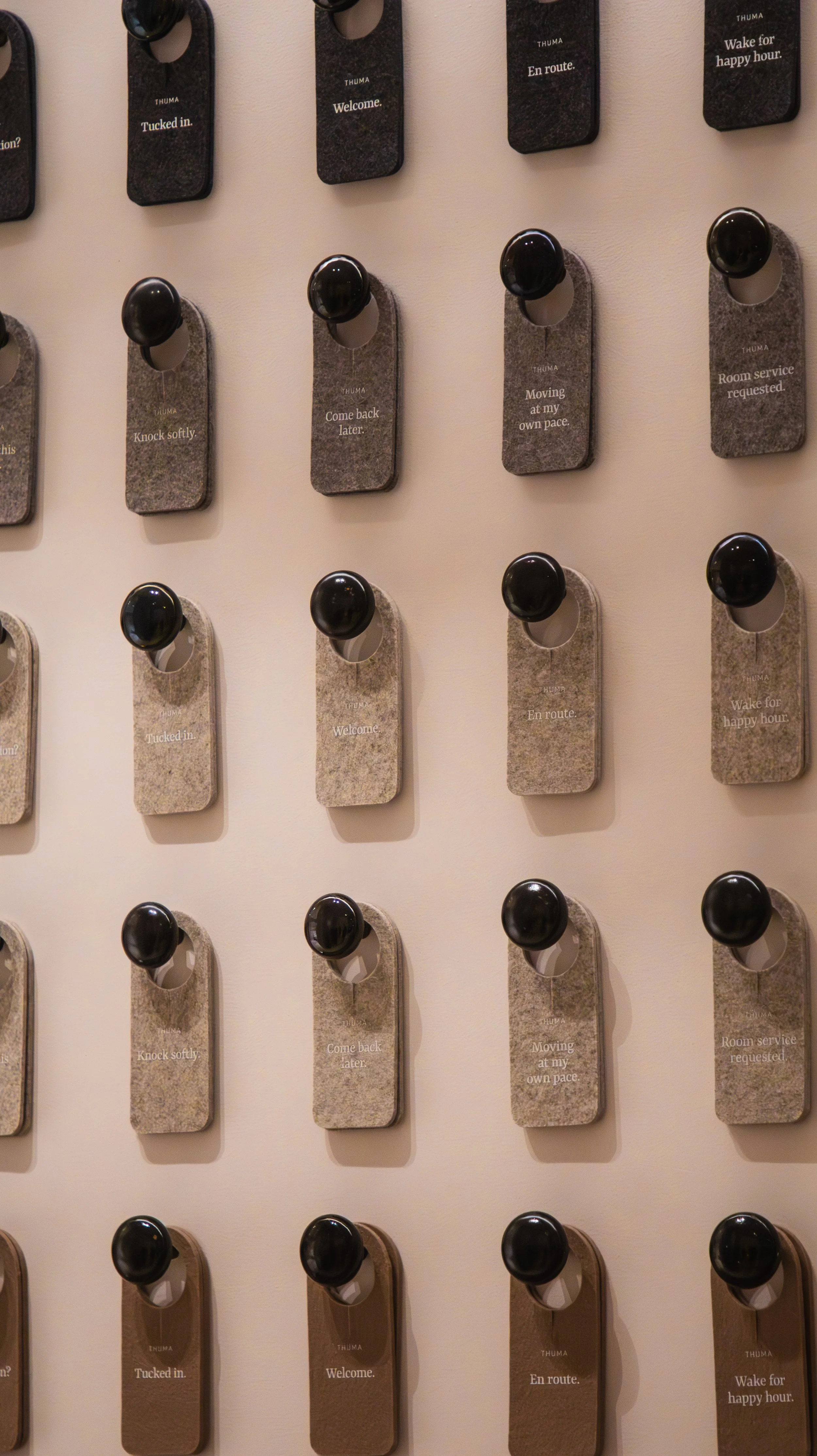 Wall-mounted hooks with black knobs on rectangular felt pads with words like 'Tucked in,' 'Welcome,' 'Come back later,' and 'Room service requested.'