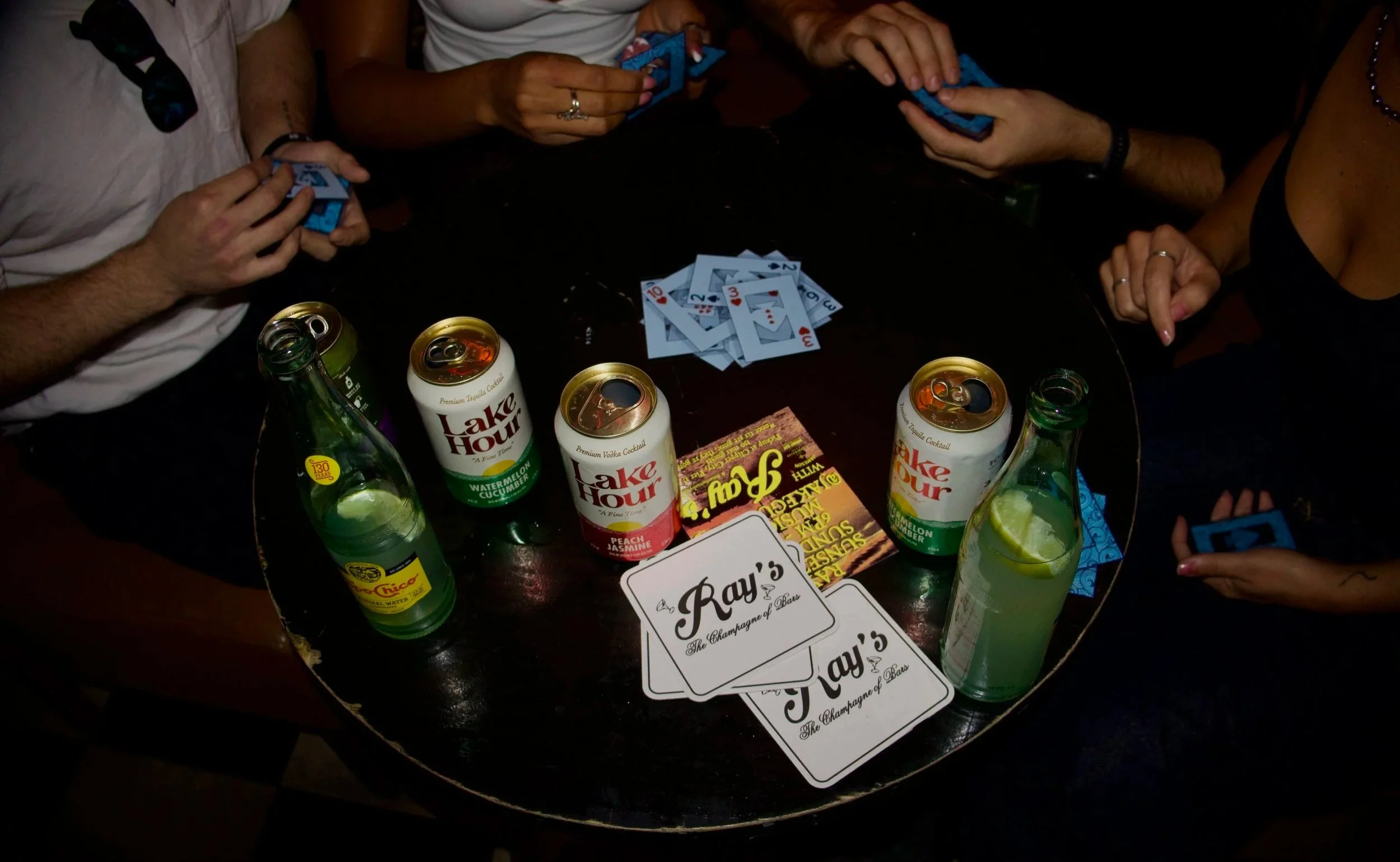 People sitting around a table playing a card game with drinks and promotional cards on the table.