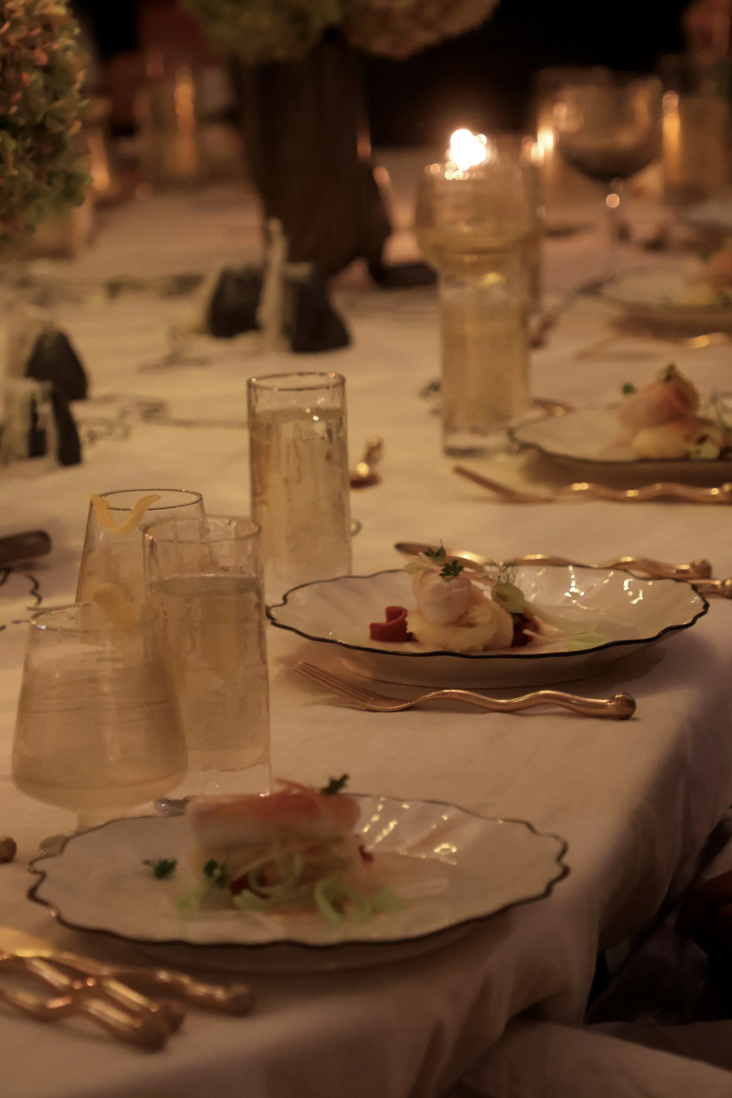 Elegant dinner setting with plates of food, glasses, and cutlery on a decorated table under warm lighting.