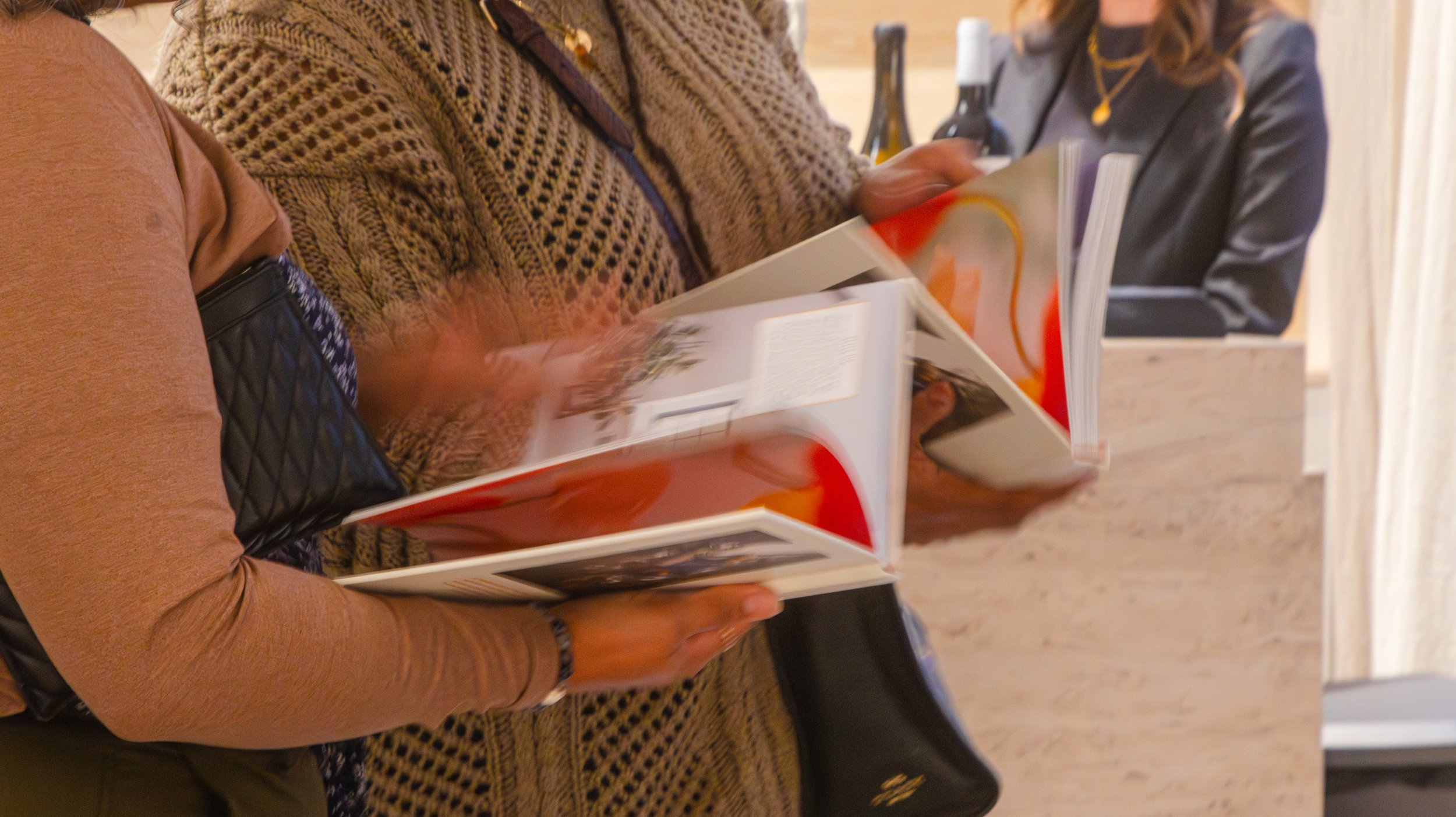 People sitting in a cafe or bookstore, looking at books or magazines on their laps or tables.