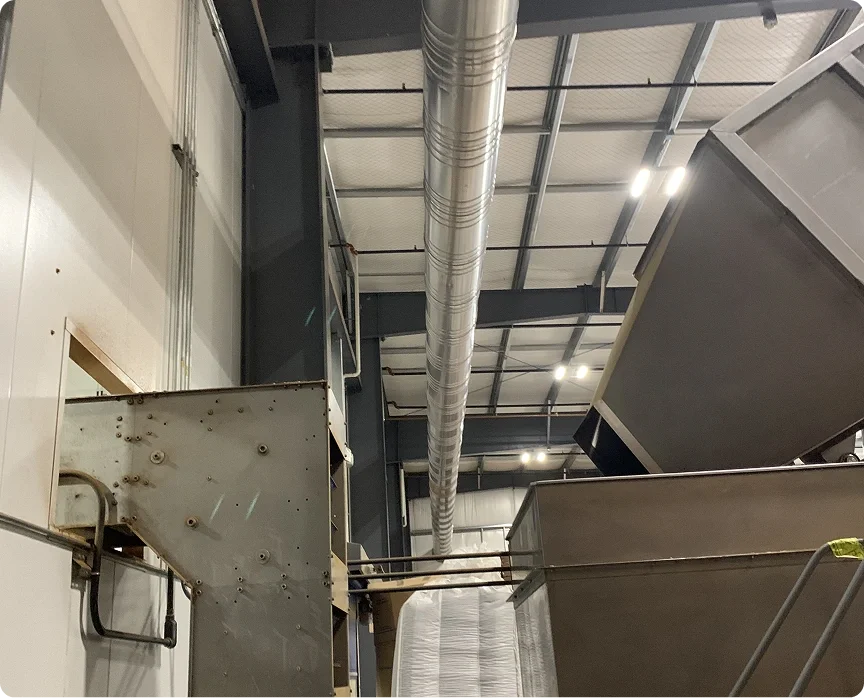 Industrial interior with large metallic ductwork, exposed structural beams, and machinery or equipment in a warehouse or manufacturing facility.