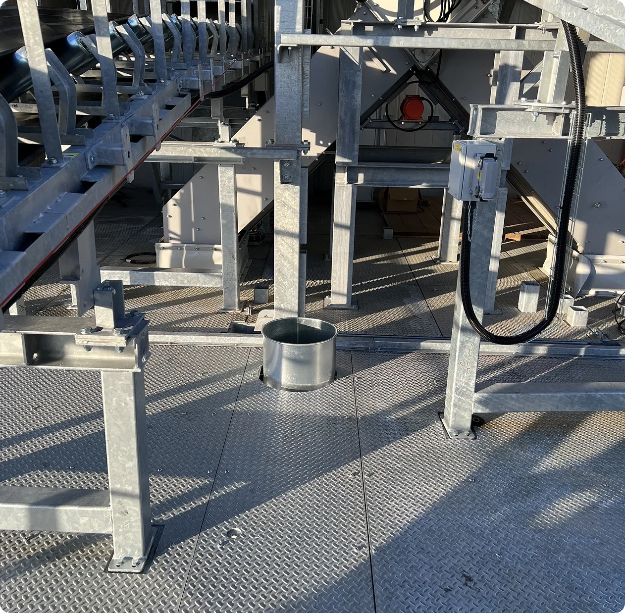 Metal platform with industrial equipment, pipes, and a small metal container on the floor.