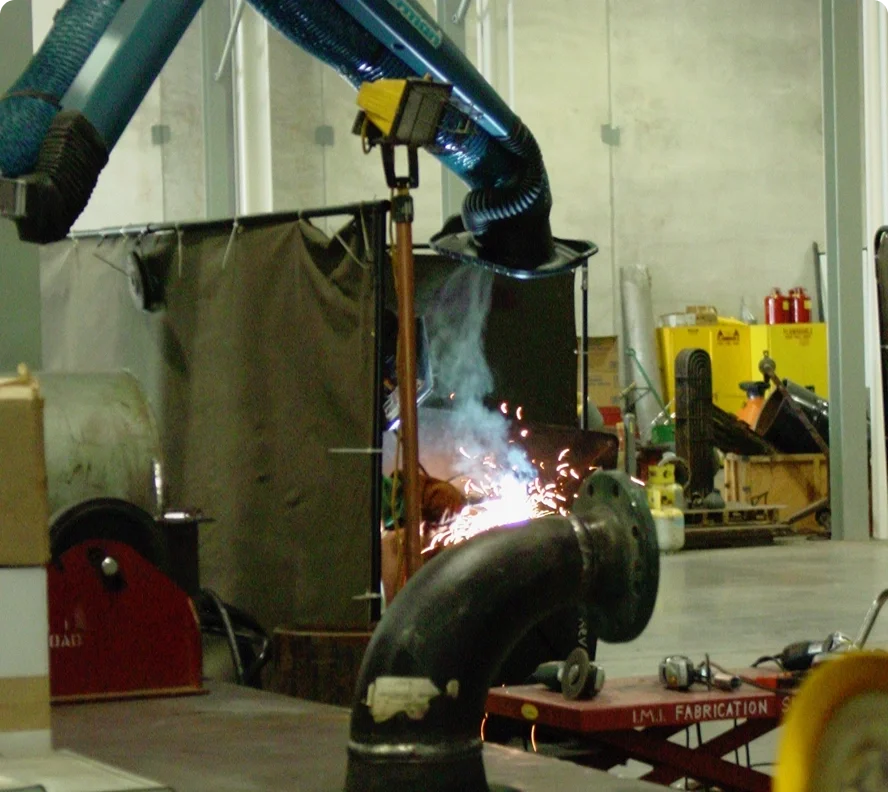 Welding in a manufacturing or industrial workshop, with sparks and smoke coming from the welding process, surrounded by equipment and tools.