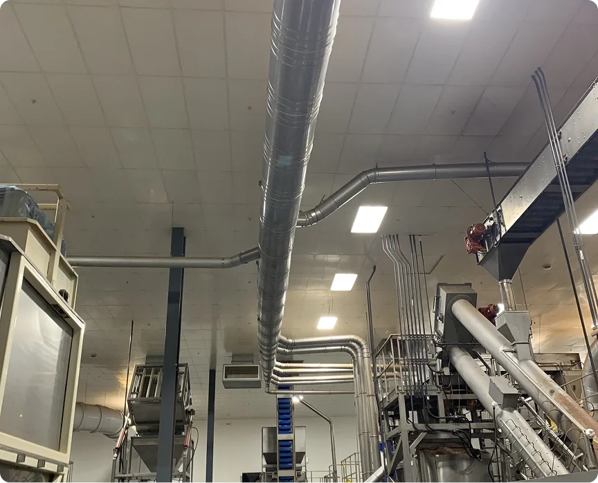 Industrial ceiling with large ventilation ducts, pipes, and equipment in a factory or processing plant.
