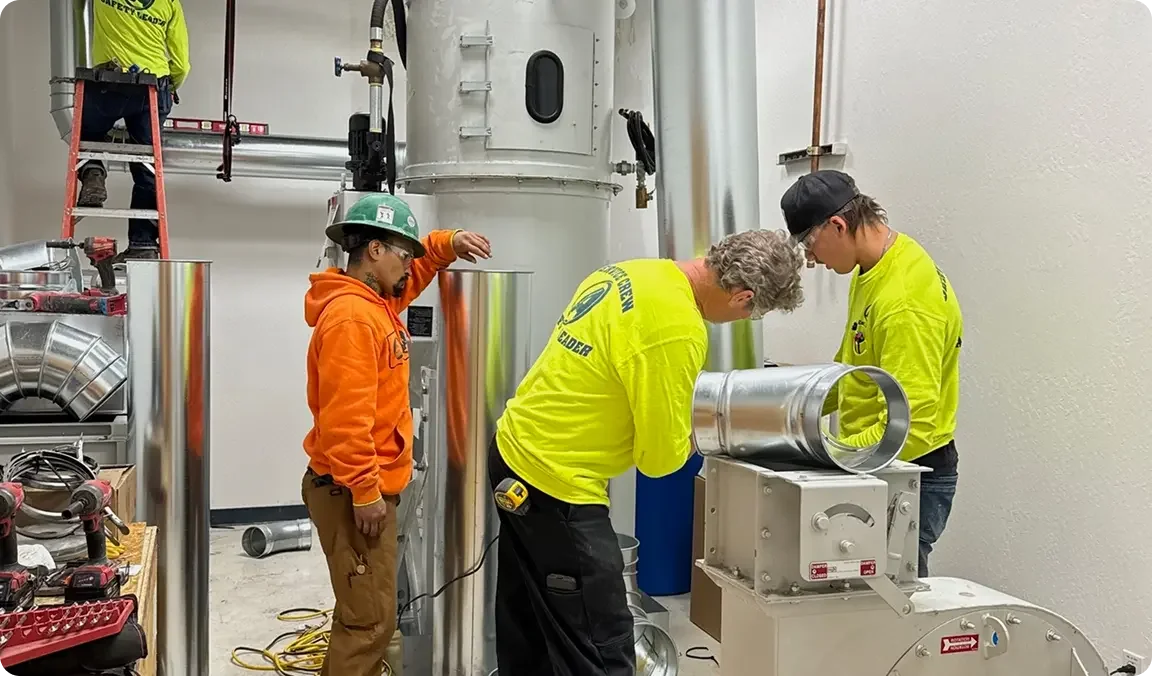 Four workers in safety gear working with metal industrial equipment in an indoor setting.