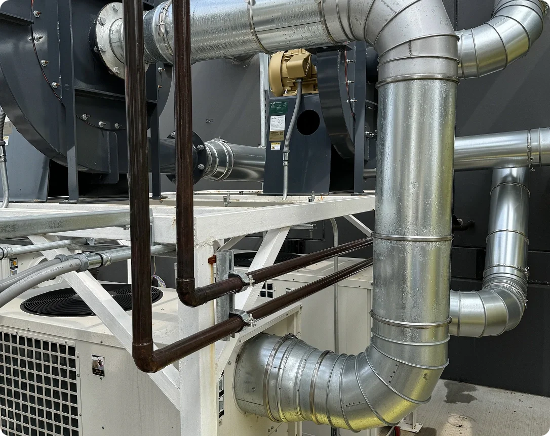 Industrial HVAC system with interconnected metal pipes and ducts, some painted black and others silver, mounted on a white metal frame.