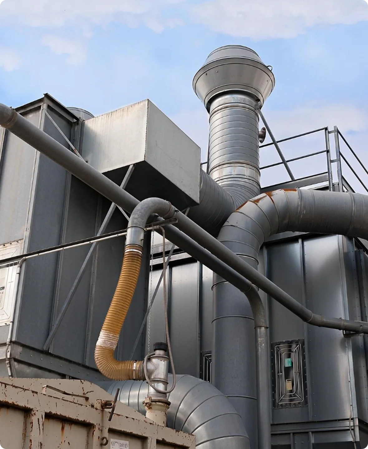 Industrial building with large metal pipes and ducts against a blue sky.