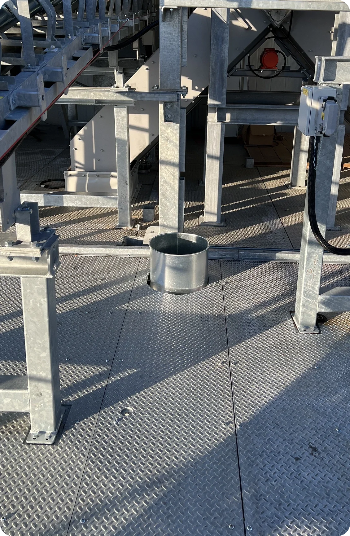 Metal platform with structural supports, a small metal cylinder, and mechanical equipment, including a red circular component, in an industrial setting.
