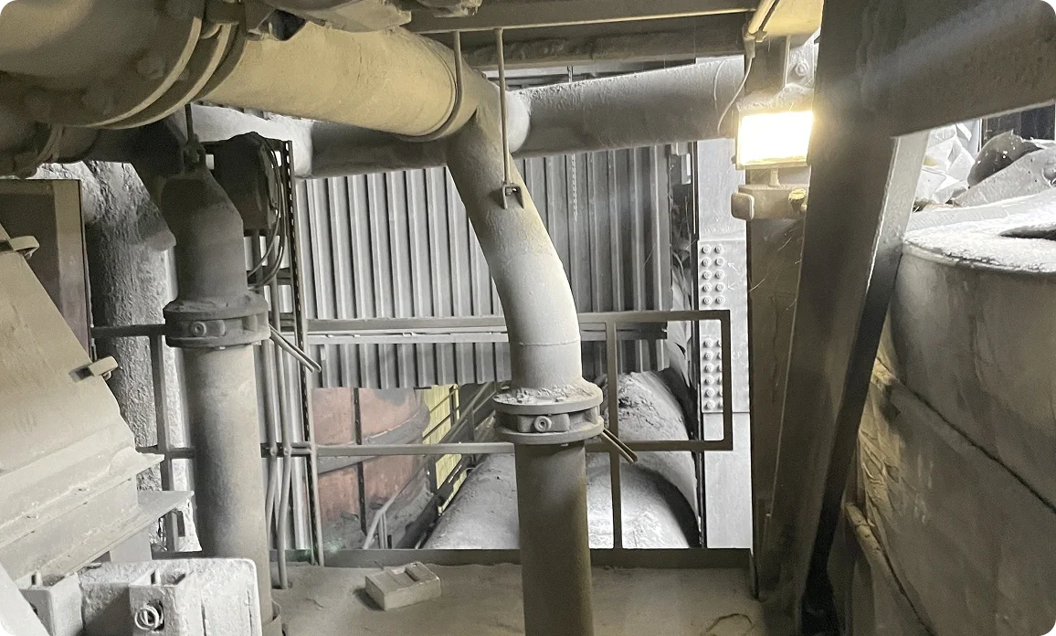Industrial pipes, valves, and metal structures in a dust-filled factory or plant environment.