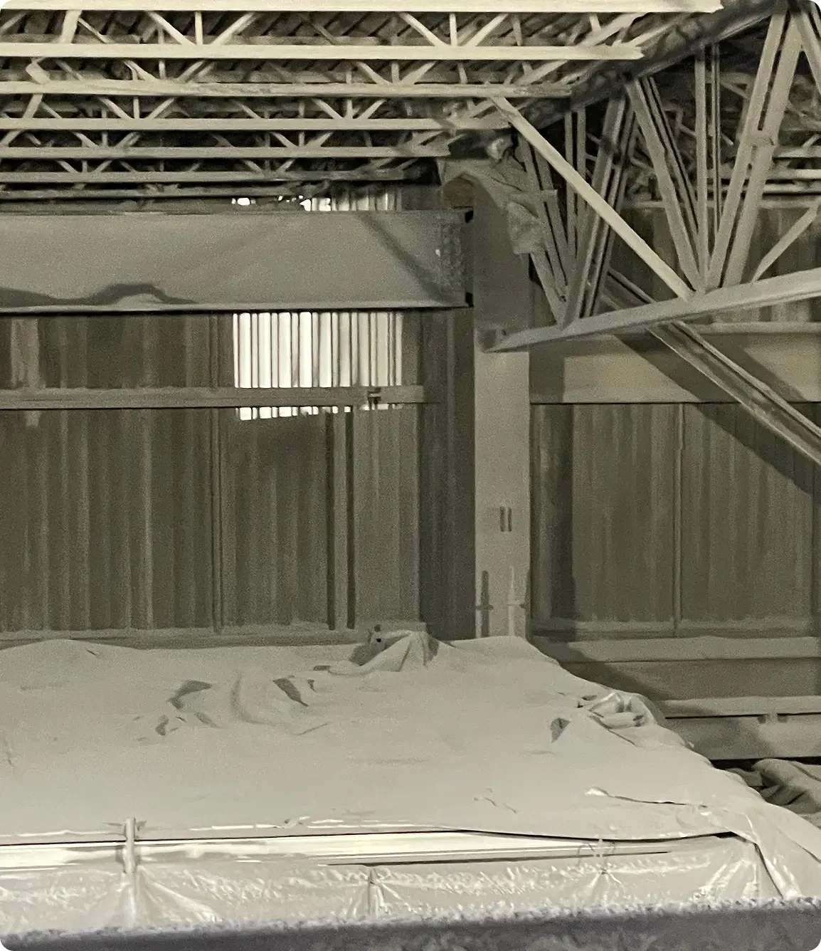 Interior view of a construction site showing steel framing, insulation, and a covered object in the foreground.