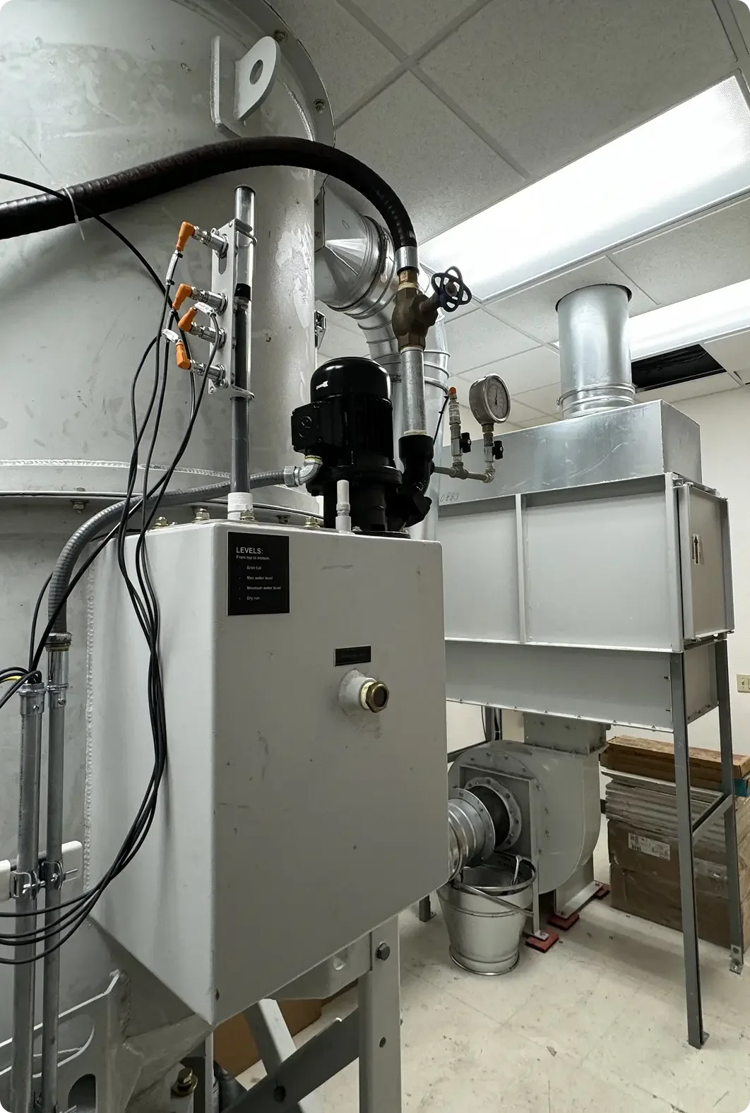 Industrial machinery with pipes, gauges, and electrical components in a laboratory or manufacturing setting.