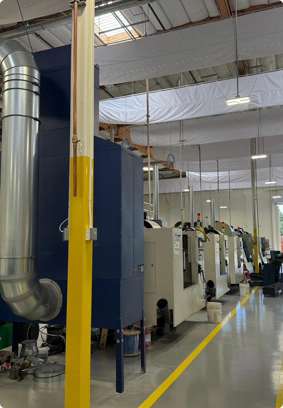 Industrial manufacturing facility with machinery, large ventilation ducts, and yellow safety markings on the floor.