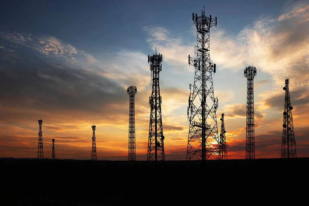 A series of communication towers silhouetted against a sunset sky with clouds.