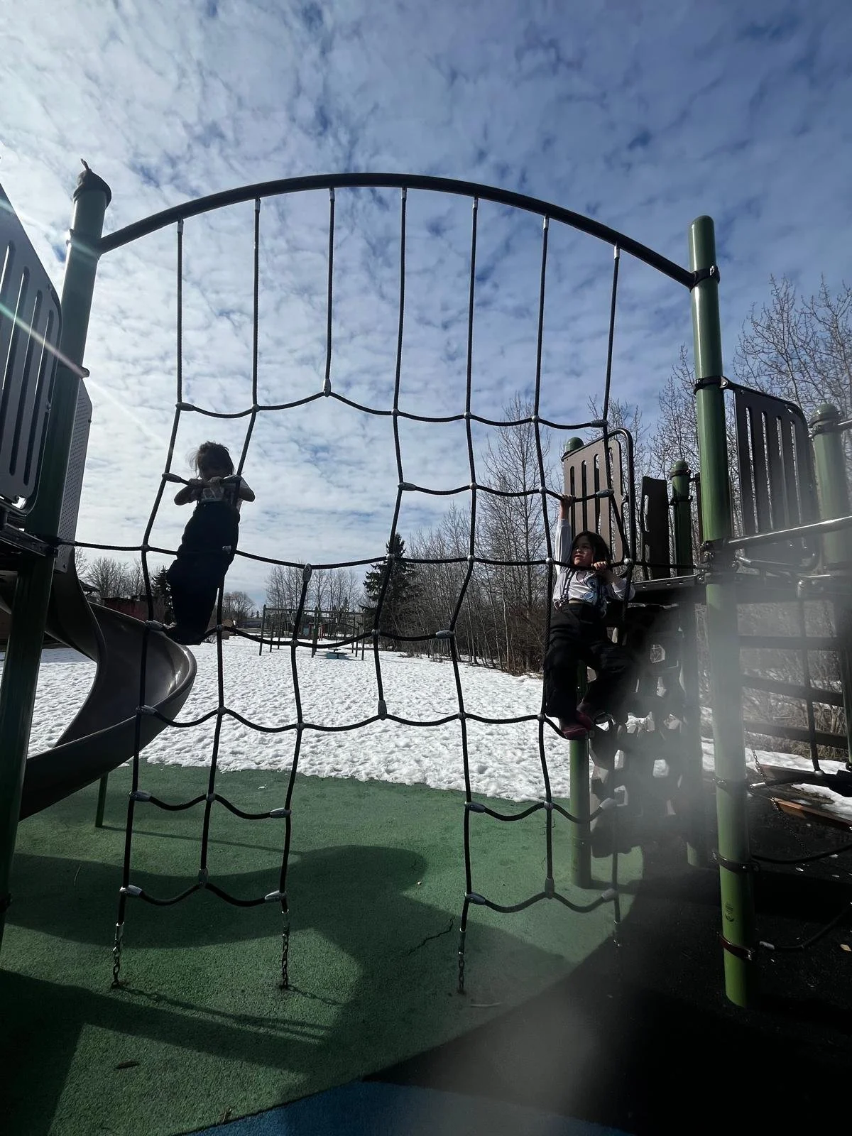 A young child climbing a rope cargo net on a snowy playground structure .