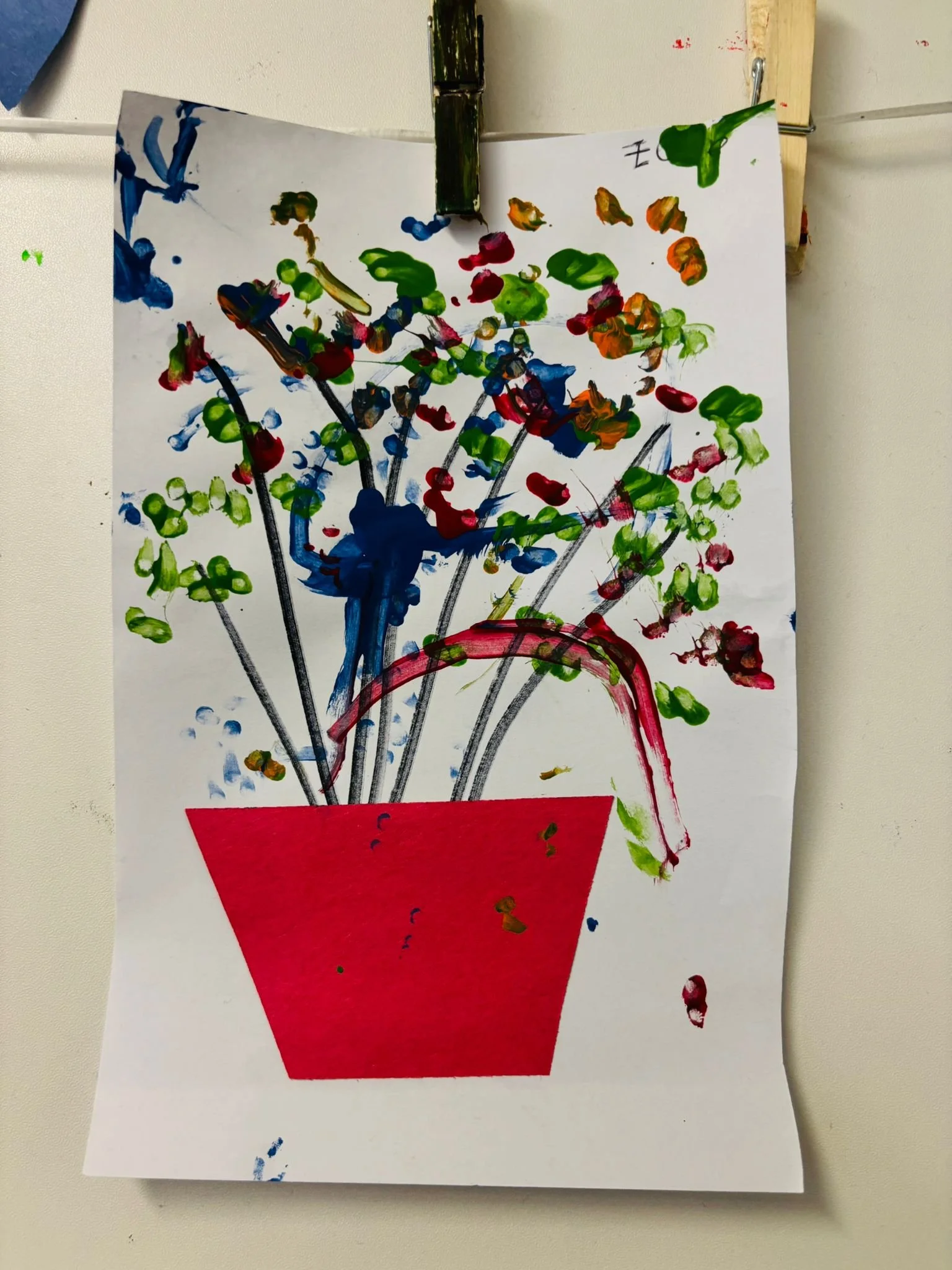 A vibrant children's painting of a red flower pot with colorful fingerprint flowers hanging up on display