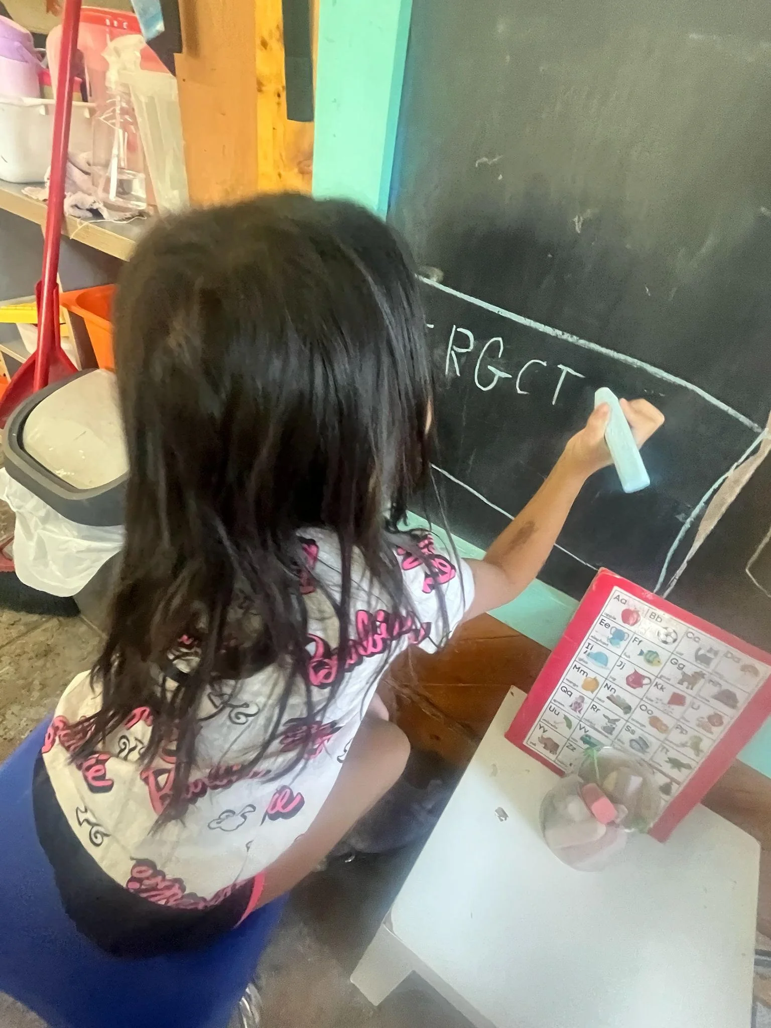 A young girl writing letters with white chalk on a blackboard.