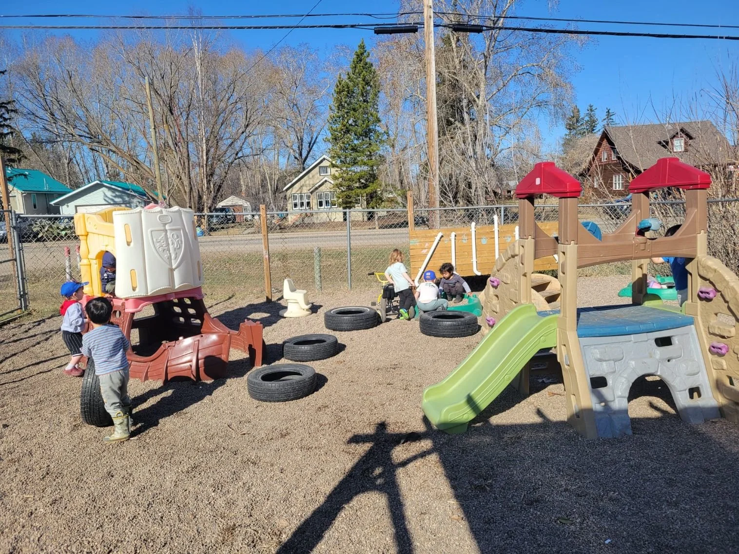 A spacious outdoor daycare playground equipped with slides, climbing structures, and toy tires on a sunny day.