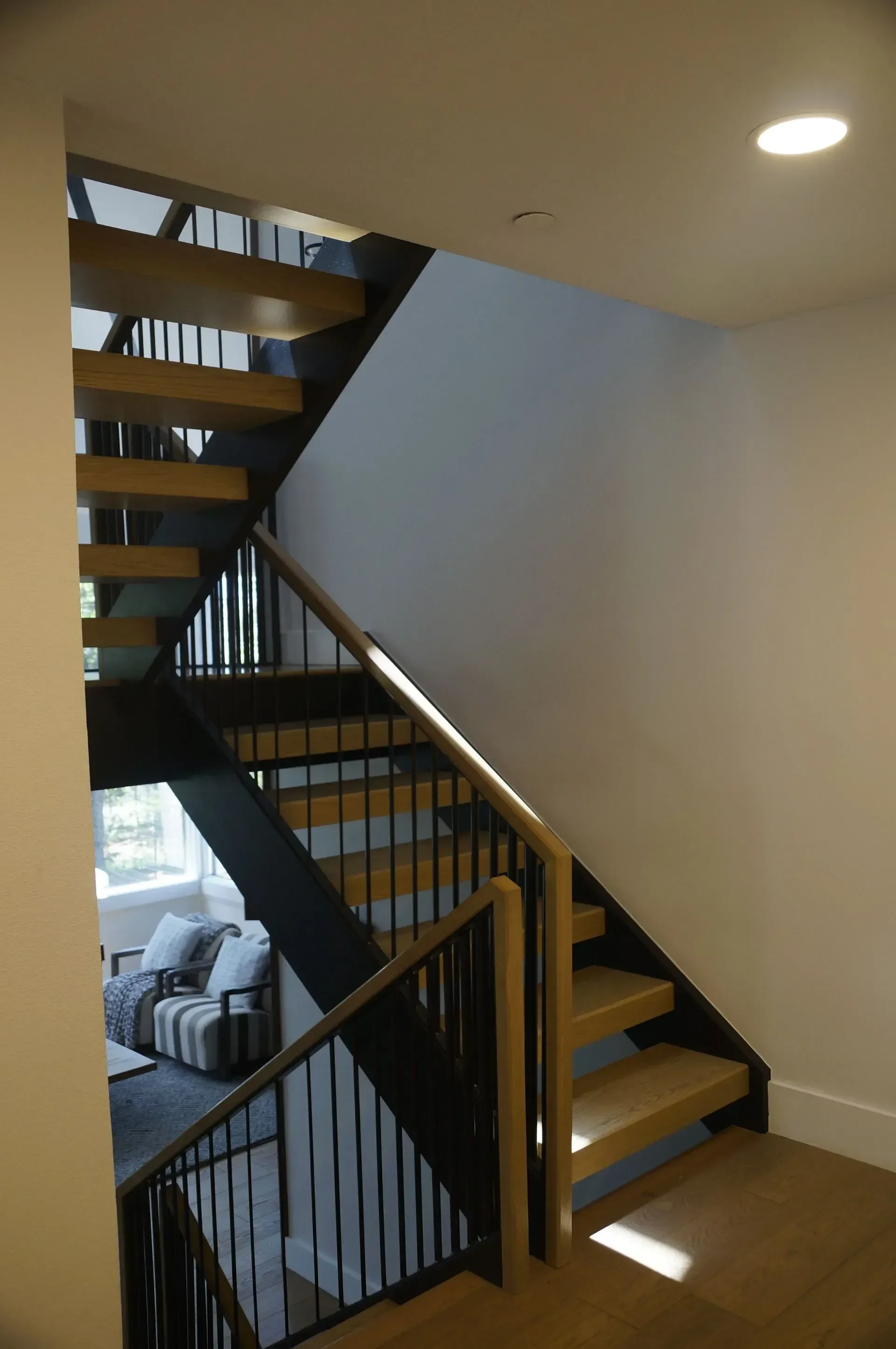 Wood and metal staircase leading down to a living room with a gray armchair and a window with trees outside.