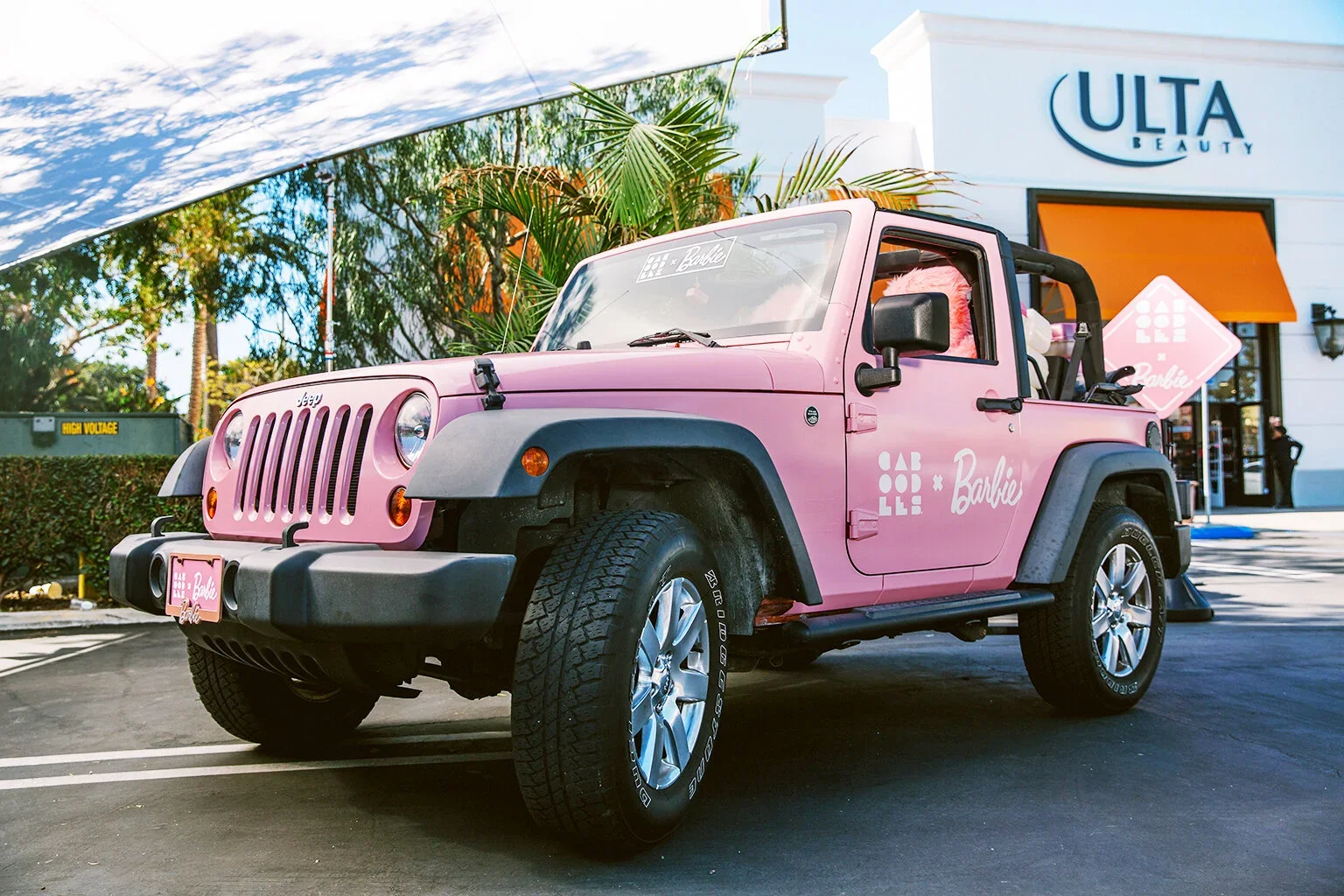 Pink Jeep with Barbie branding parked outside Ulta Beauty store, decorated with Barbie logos and accessories, under a clear sky.