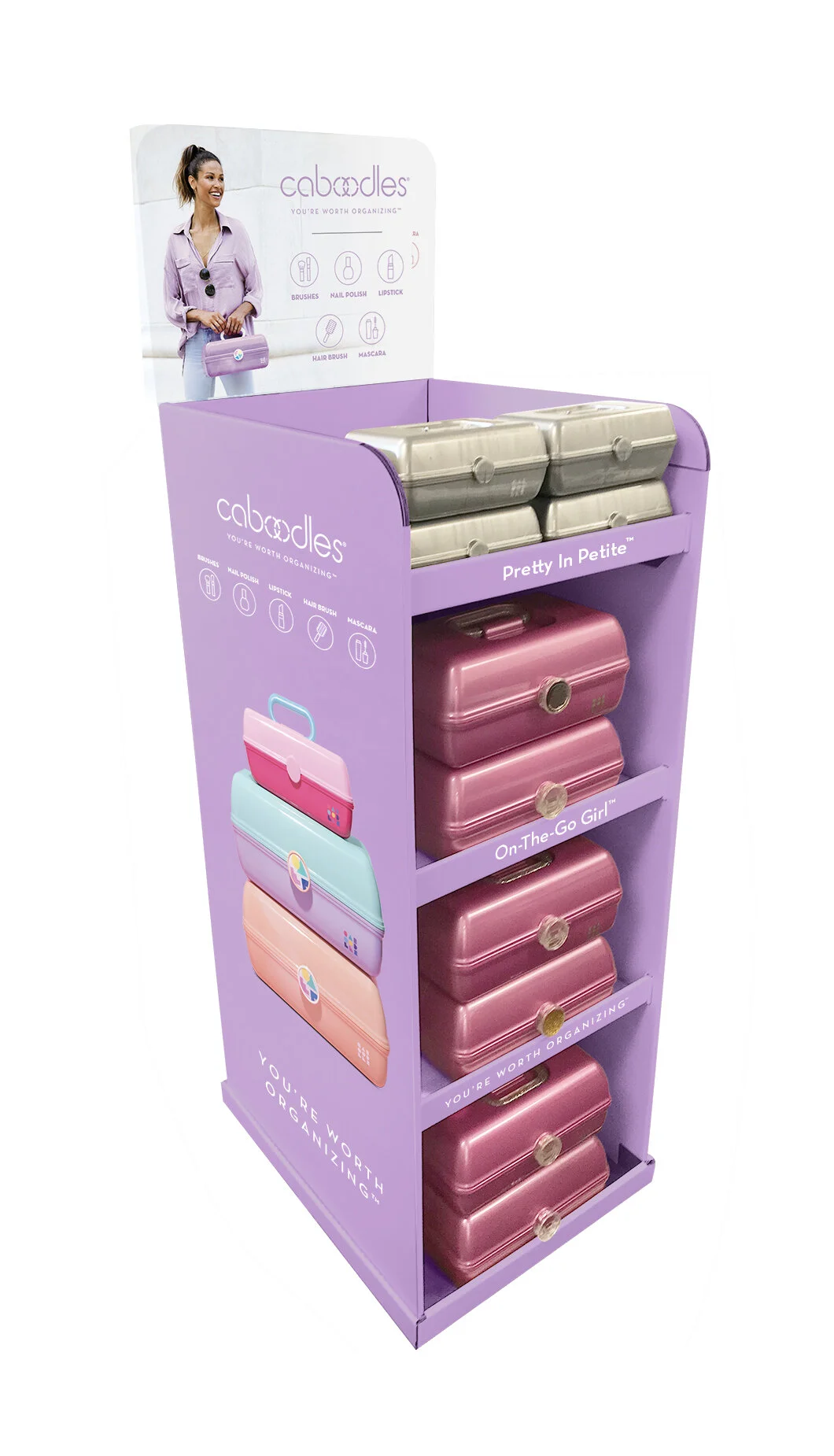A purple organization display rack with multiple small compartments containing pink and beige cases, labeled 'Pretty In Petite,' 'On-The-Go Girl,' and 'You're Worth Organizing,' featuring images of colored bags on the side, and an overhead sign for Caboodles brand.