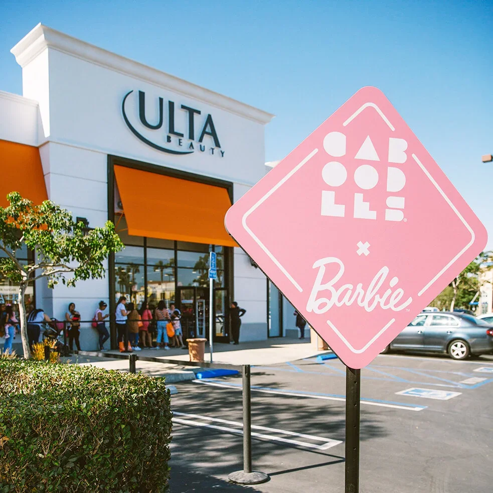 Queue of people waiting outside Ulta Beauty store with a pink sign promoting a Barbie-themed event or collaboration.