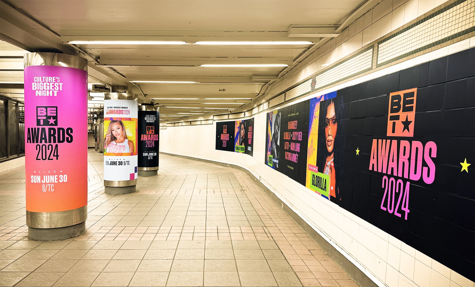 Interior view of an underground tunnel or subway station decorated with colorful posters advertising the BET Awards 2024 happening on June 30 at 8/7c.