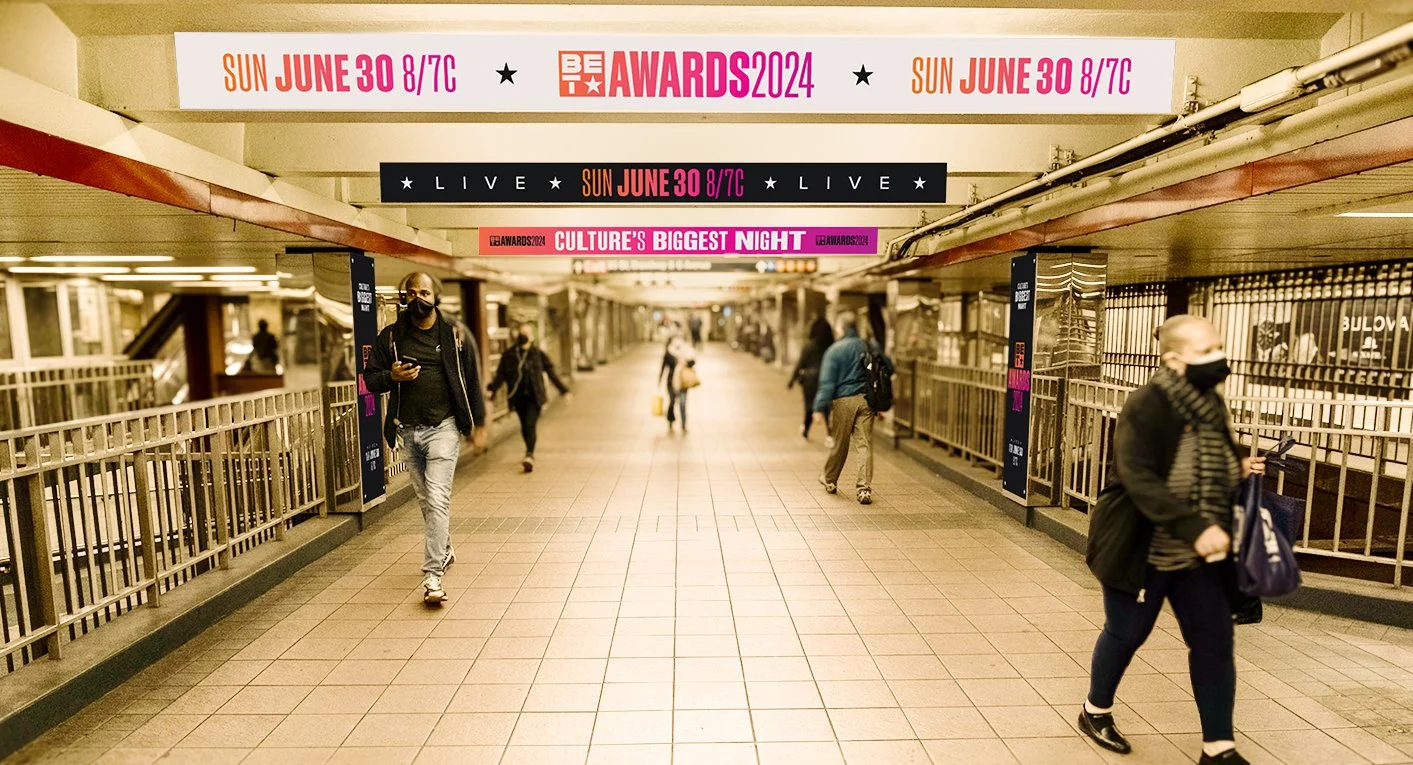 Underground transit station corridor with people walking, some wearing masks. Overhead signs advertise the BET Awards 2024 on Sunday, June 30 at 8/7c.