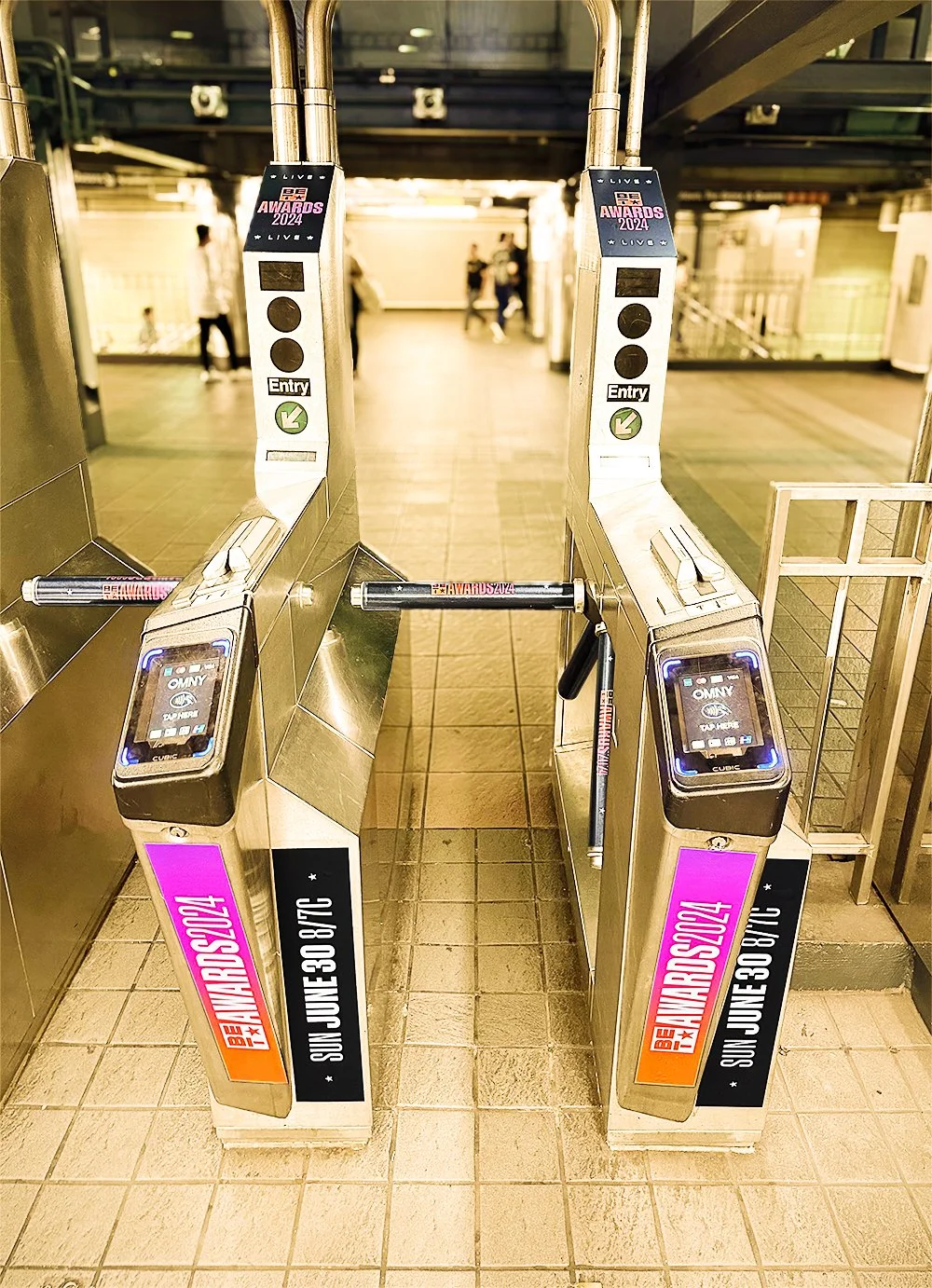 Two metal turnstiles with digital card readers, set for entry and dated for the 2024 BET Awards, located in an indoor public space.