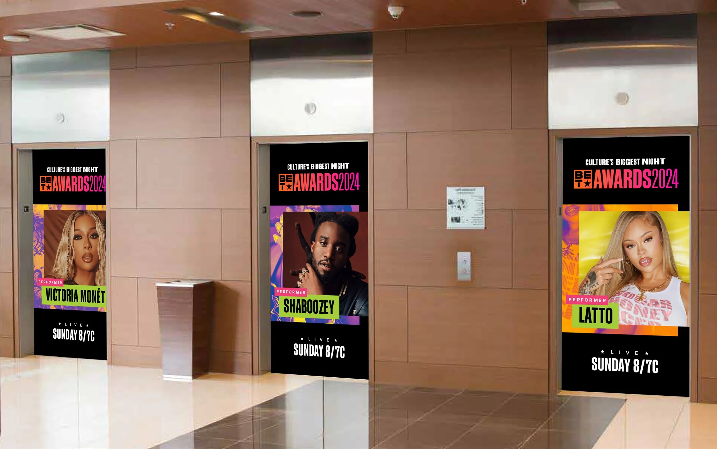 Posters in an elevator lobby advertising a live music event featuring performers Victoria Monét, Shaboozey, and Latto, airing on Sunday at 8/7c.