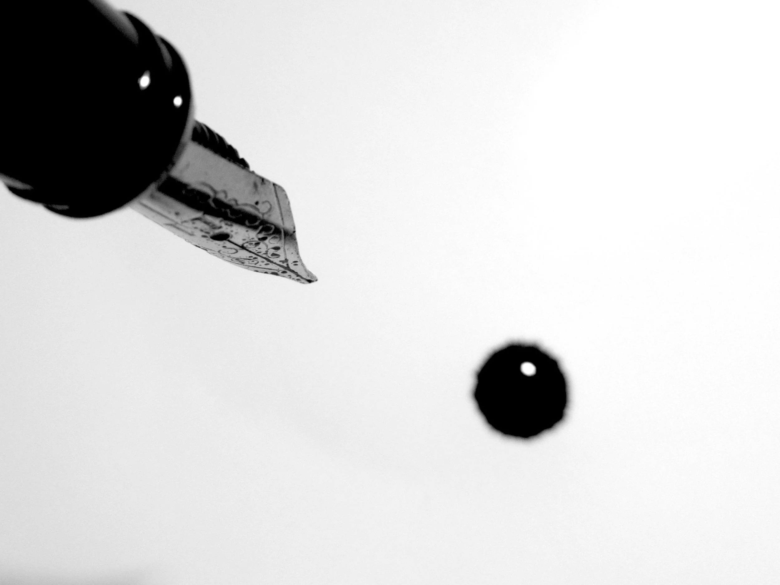 Close-up of a fountain pen nib, with a blurred dark object in the background against a light surface.