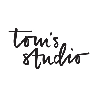 Logo with the text 'tom's studio' in black, handwritten-style font on a white background.