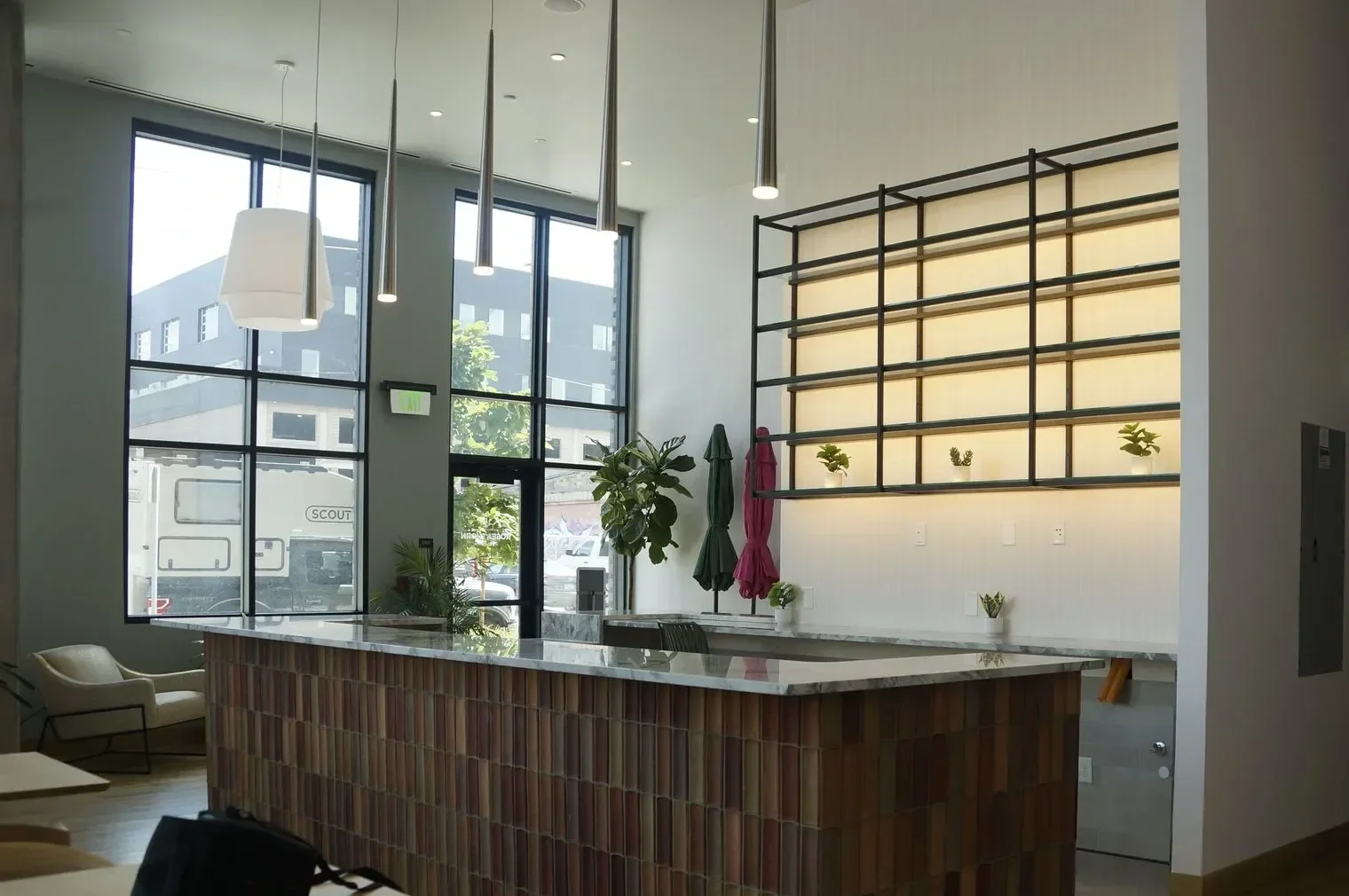 Modern cafe interior with a marble countertop, large windows, hanging pendant lights, and decorative plants.