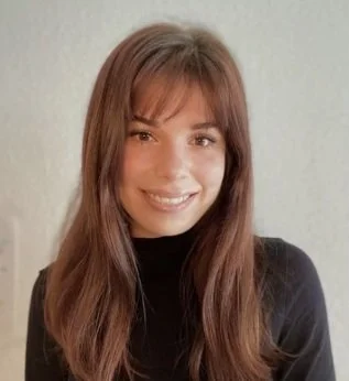 A young woman with long brown hair and a black top smiling at the camera