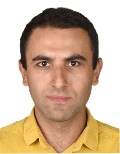 Portrait of a man with short dark hair, wearing a yellow shirt, against a white background.