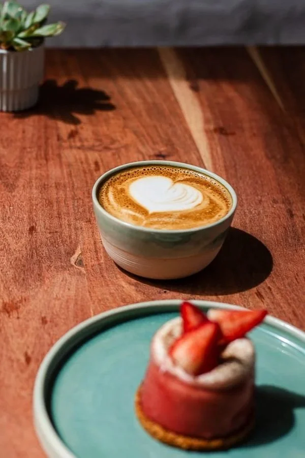 Tasse de café avec de la mousse en forme de cœur et un dessert à la fraise sur une assiette, de chez Xocolatte à Lille