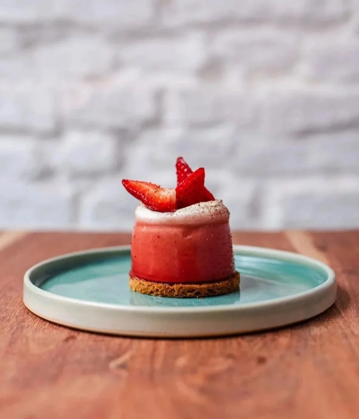 Dessert de chez Xocolatte à Lille, avec des fraises tranchées et de la crème, présenté sur une assiette pêche, posé sur une table en bois, fond flou blanc.