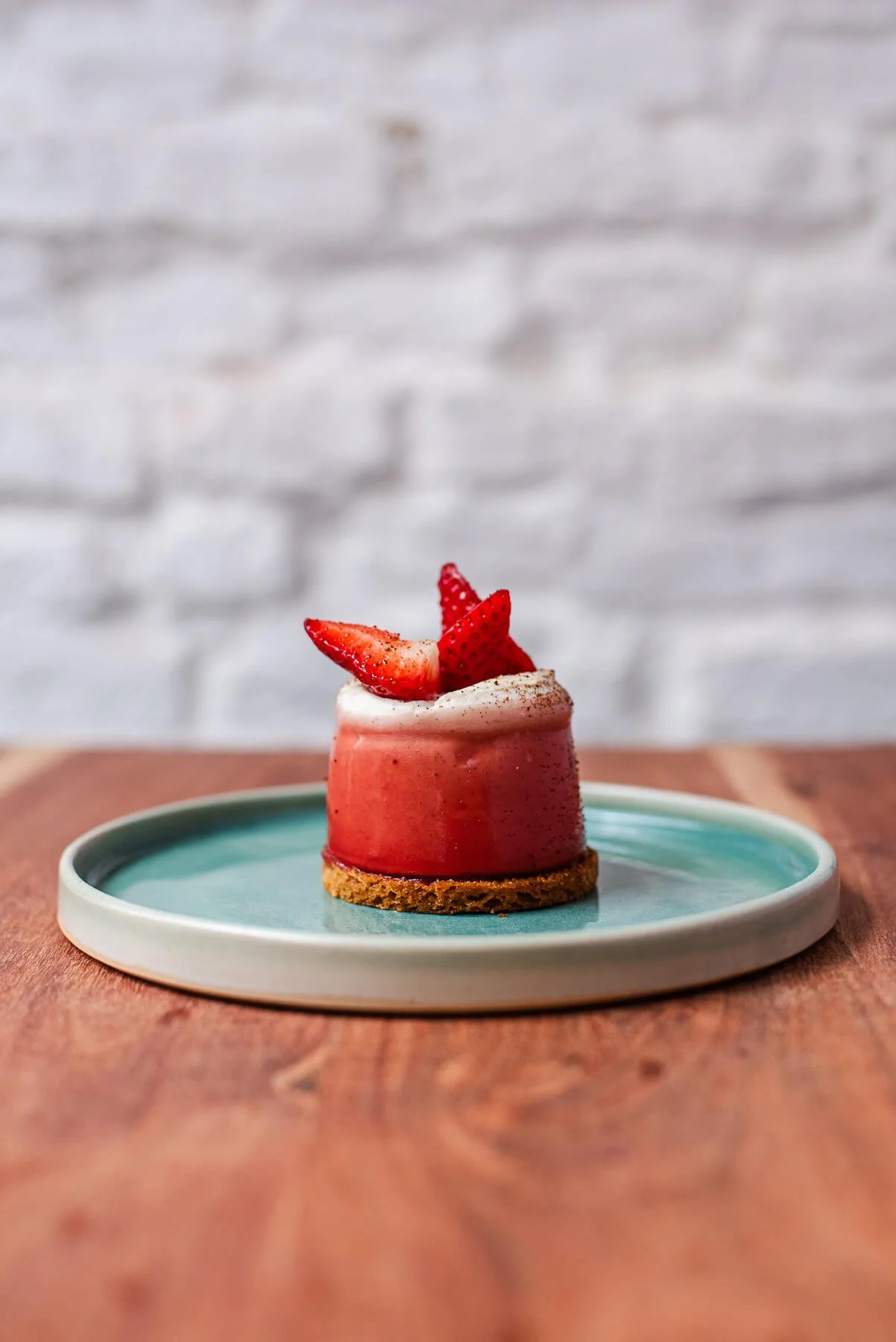Un dessert avec des fraises de chez Xocolatte à Lille, présenté sur une assiette bleue sur une table en bois avec un mur blanc en arrière-plan.