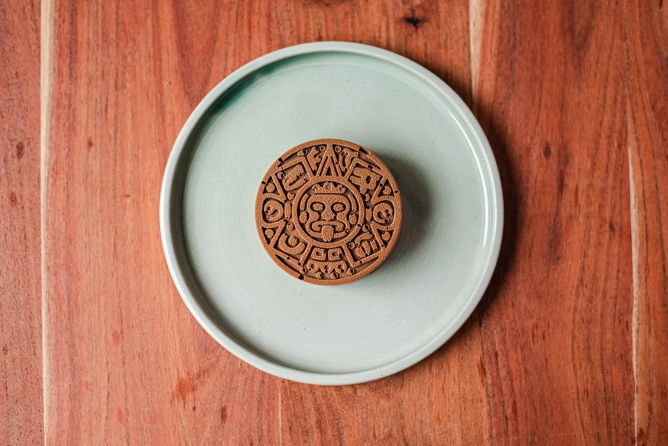 Disque de chocolat avec motifs moulés, placé dans une assiette verte sur une surface en bois, de chez Xocolatte à Lille