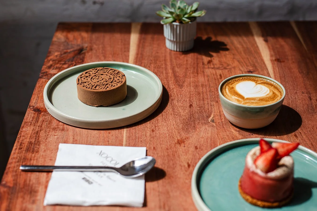 Gâteau au chocolat rond, mousse de café avec cœur en latte art, gâteau roulé à la fraise dans une assiette verte, de chez Xocolatte à Lille