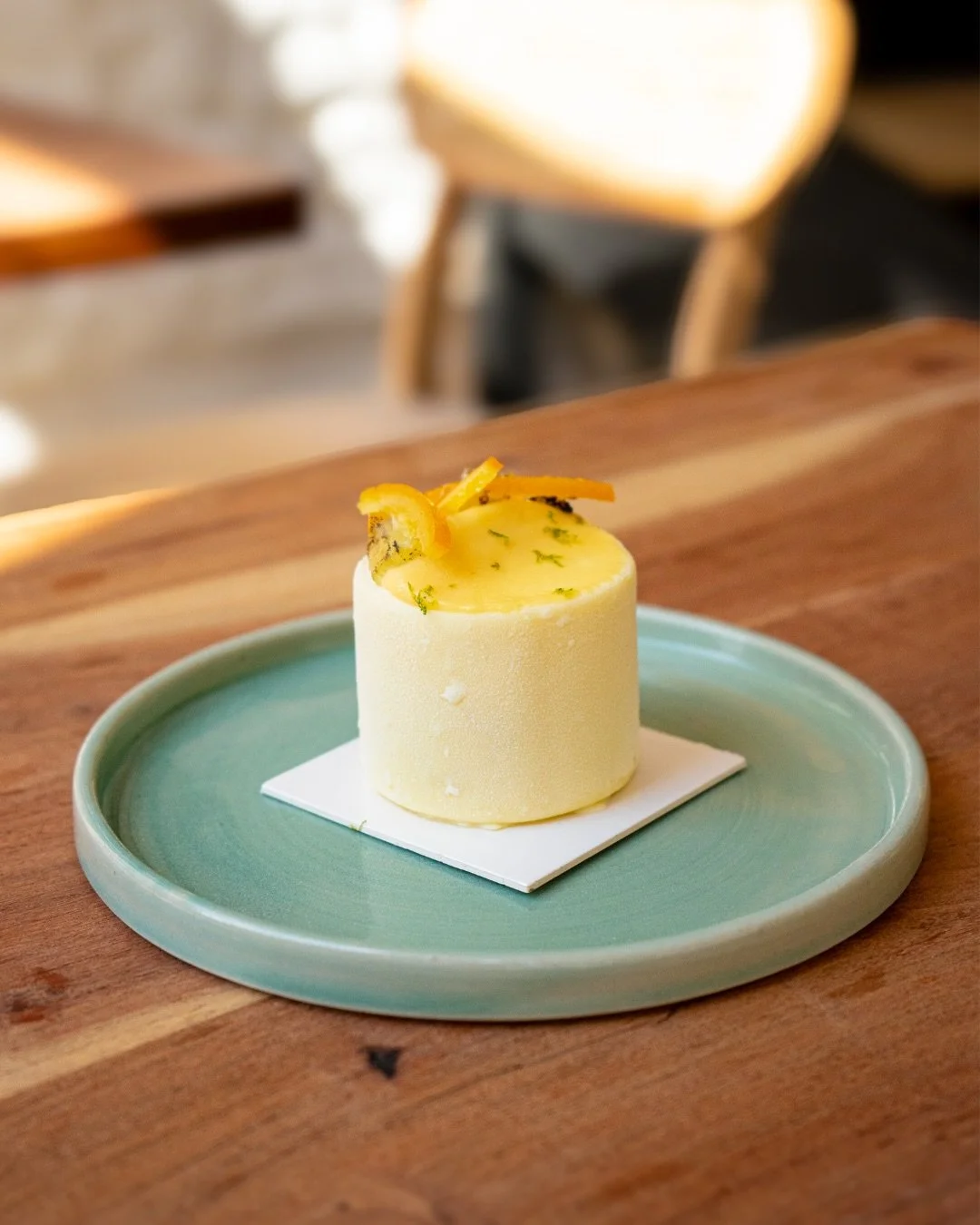 Dessert cylindrique avec des zestes d'agrumes, présenté sur une assiette verte de chez Xocolatte à Lille
