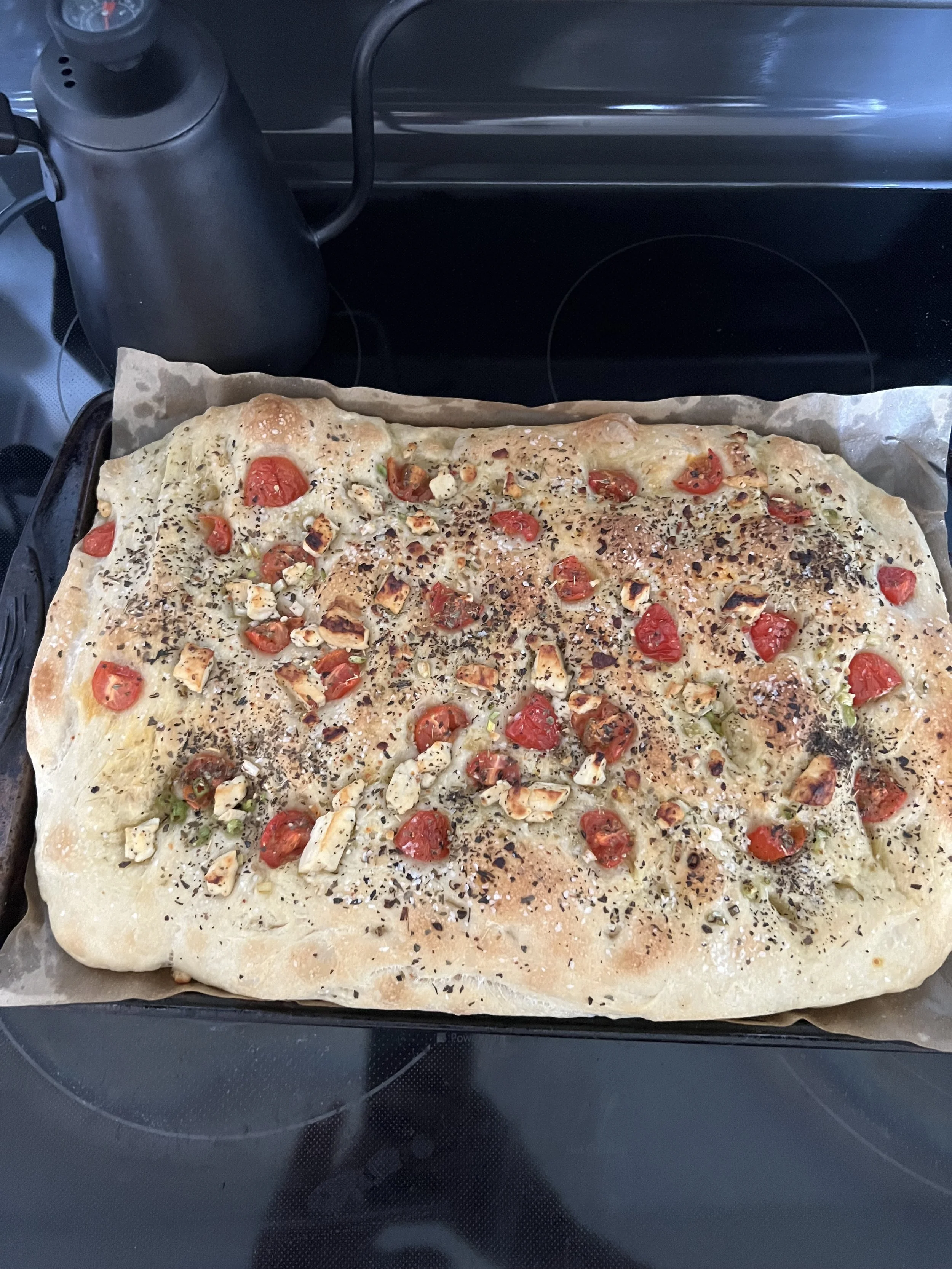 Uncooked homemade flatbread pizza topped with cherry tomatoes, chopped garlic, herbs, and black pepper on parchment paper, resting on a baking sheet.