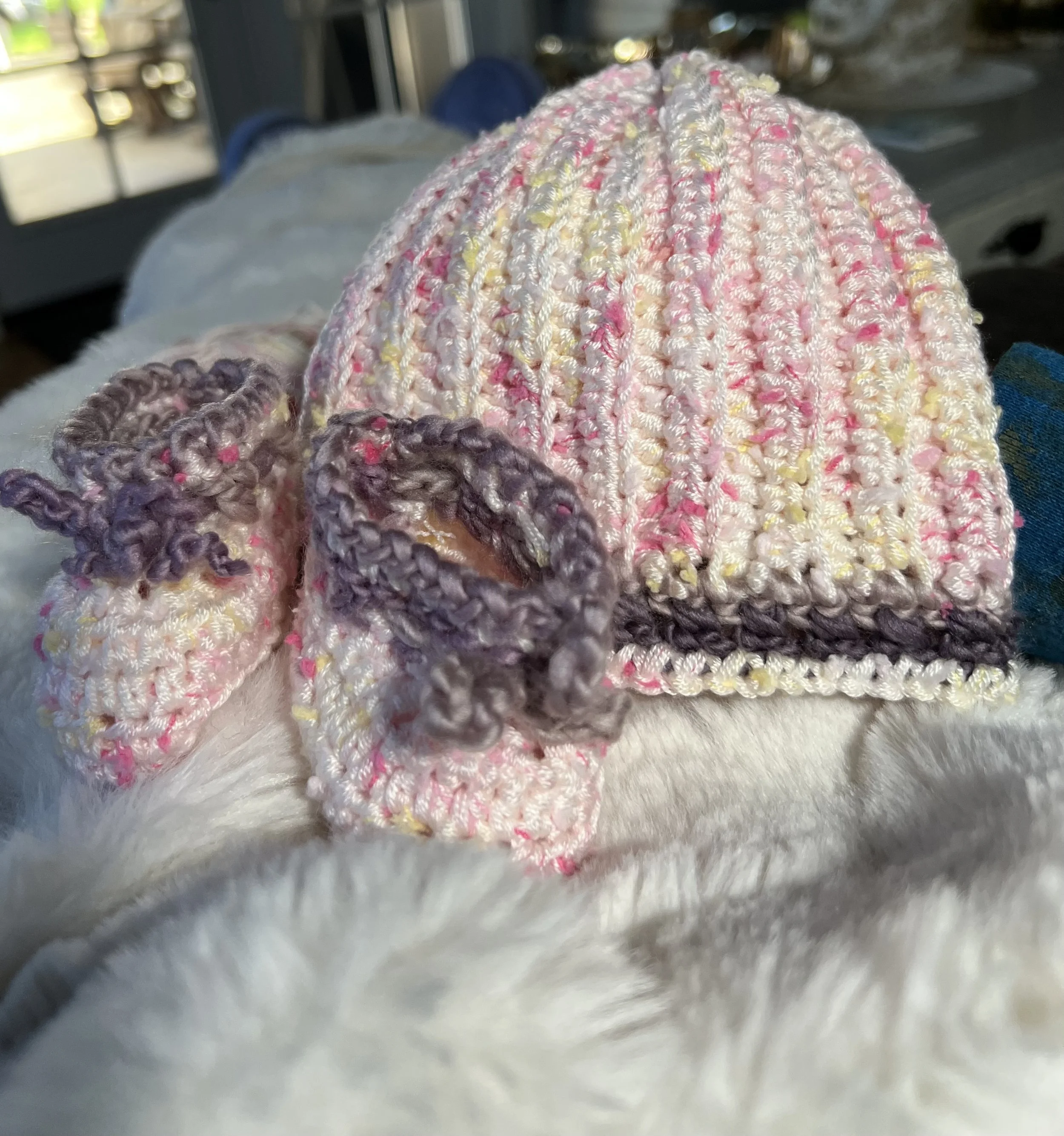 Close-up of colorful handmade crocheted hats, with pink, yellow, and purple yarn, on a light-colored surface. Salem, Oregon. Marion County, Polk County, Birth Doula